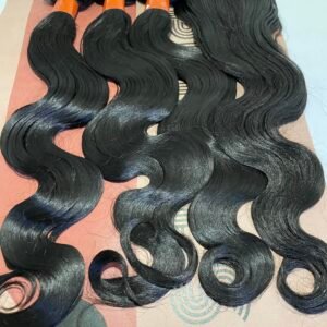 Several long, glossy black hair extensions with orange bands, laid in a row on a pink patterned surface.