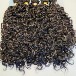 Close-up of black, tight-curled hair extensions in bundles laid on a white surface, with blue packaging visible at the top.