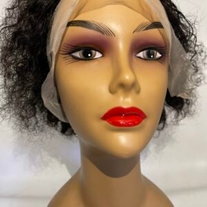 Mannequin head wearing a dark curly wig with a sheer net cap and dramatic makeup: bold red lips and sharply lined eyes.